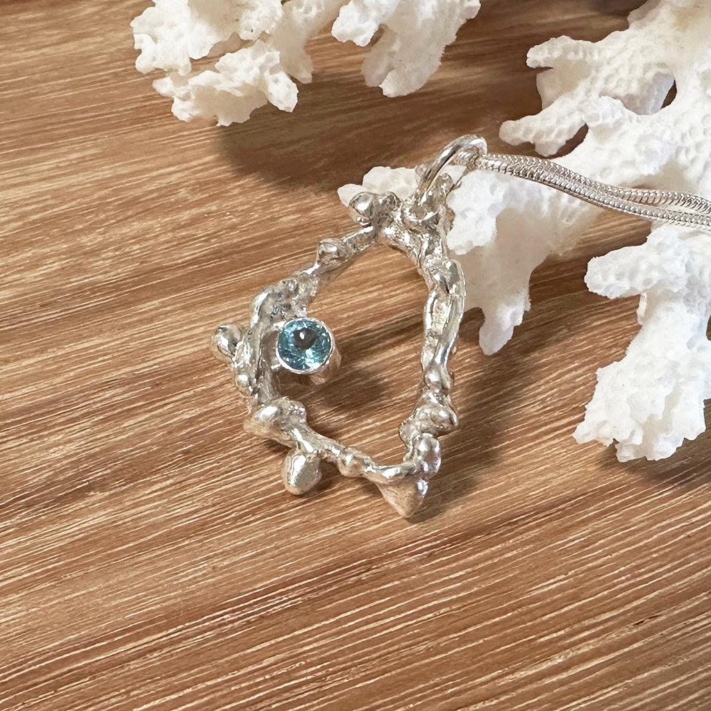 Handcrafted Argentium silver coral pendant featuring intricate branch-like texture with blue topaz gemstone, displayed on driftwood background, on a silver snake chain. Ocean-inspired ethical jewelry by Coastalstyle Australia