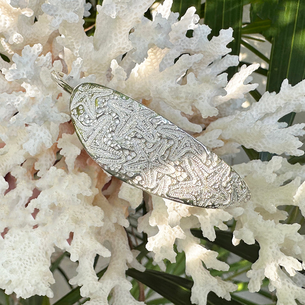 Silver cuff bracelet displayed on piece of cora, adorned with little sea stars