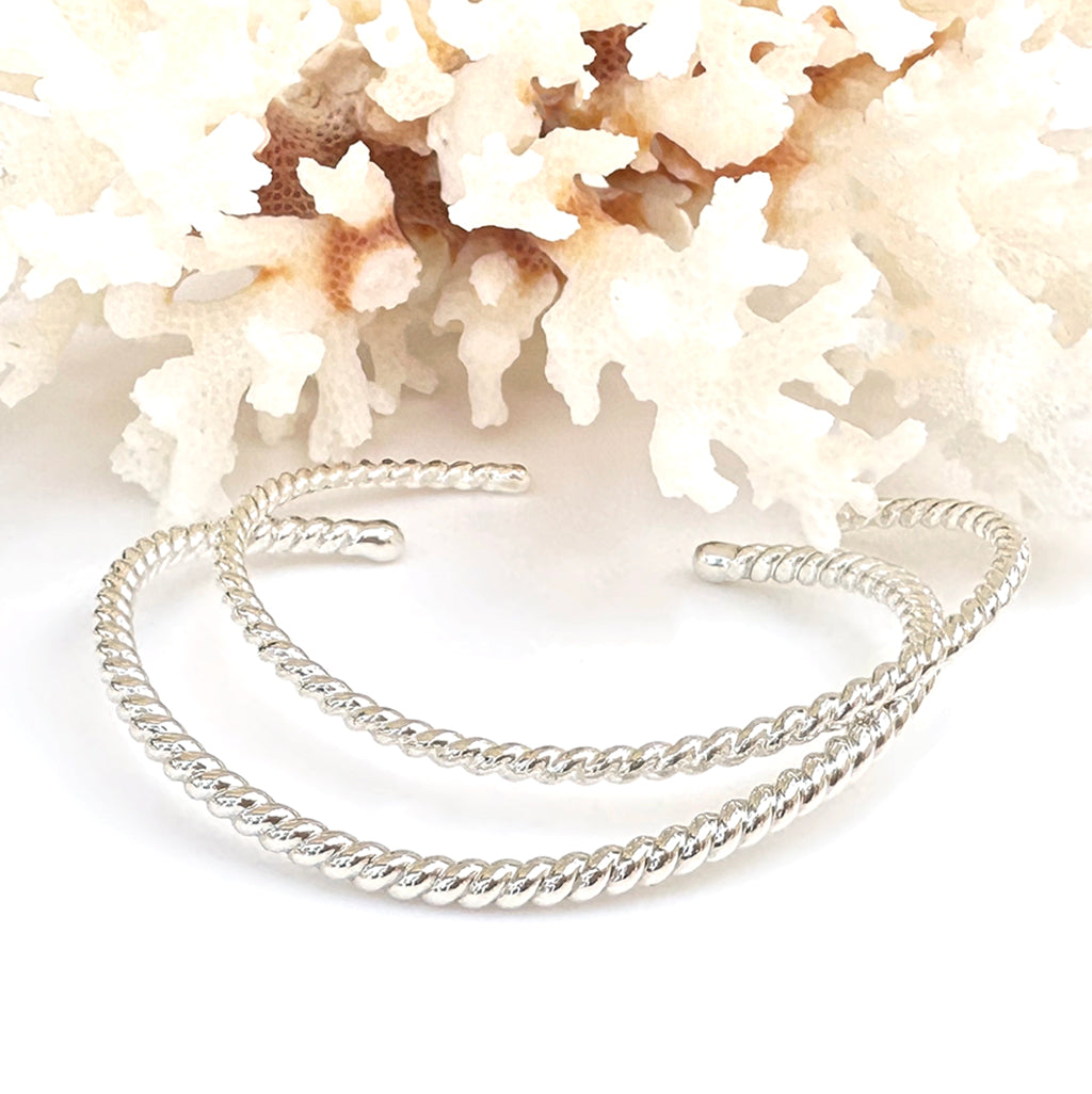 Ethically handcrafted Argentium silver stacking cuff bracelets with hammered wave-inspired textures, shown worn as a set on wrist against neutral background