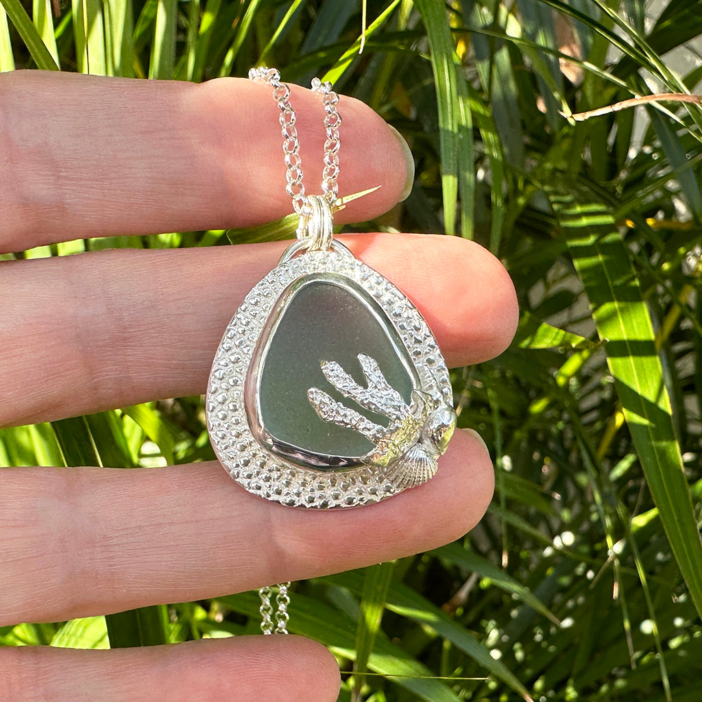 Handcrafted Aqua Mist Sea Glass pendant  bezel set in Manta Ray textured recycled fine silver. Ocean-inspired jewellery by Coastalstyle Australia displayed against neutral background on a piece of coral