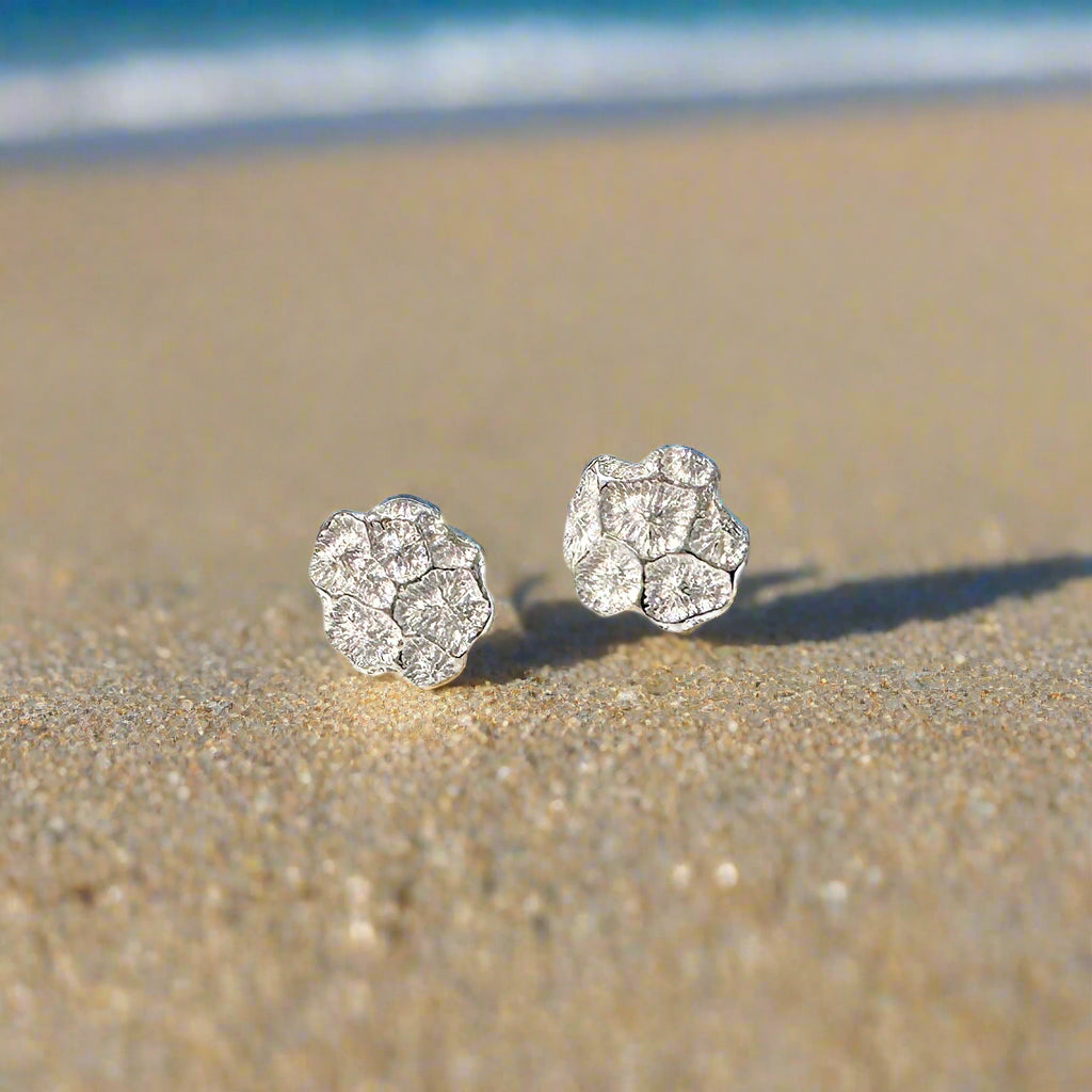 A pair of silver stud earrings with an organic, freeform shape, displayed alongside a dried coral piece.