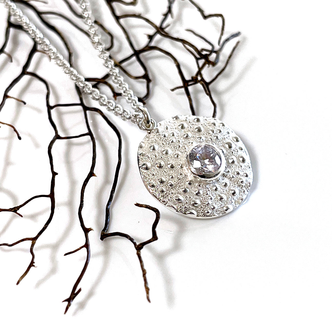 Pure silver Sea Urchin Under the Reef Necklace resting on a seashell-inspired background