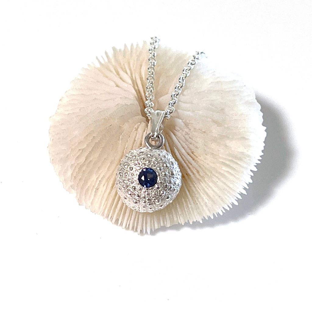 Close-up of handcrafted pure silver Baby Sea Urchin Necklace with blue lab sapphire, on a neutral background, reflecting coastal elegance.
