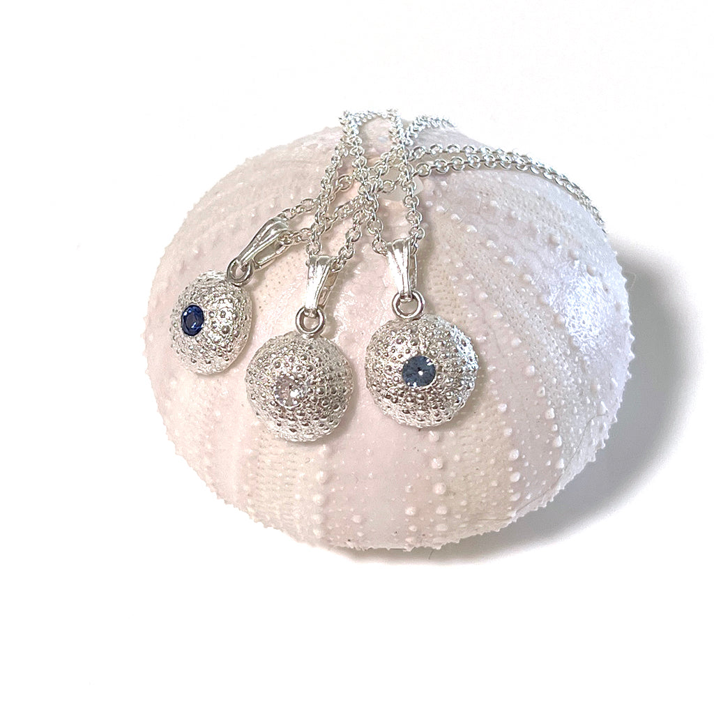 Close-up of handcrafted pure silver Baby Sea Urchin Necklaces, on pink shell, reflecting coastal elegance. Coastalstyle Australia elegance