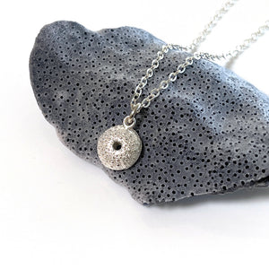 Handcrafted pure silver Sea Urchin Necklace featuring detailed texture moulded from real urchin shell, suspended on sterling silver chain on a piece of blue coral with white background. Ocean-inspired jewellery by Coastalstyle Australia.