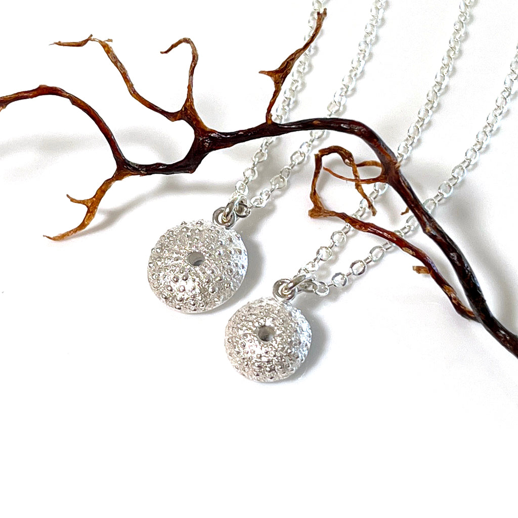 Handcrafted pure silver Sea Urchin Necklace featuring detailed texture moulded from real urchin shell, suspended on sterling silver chain on white background with small coral branch. Ocean-inspired jewellery by Coastalstyle Australia.