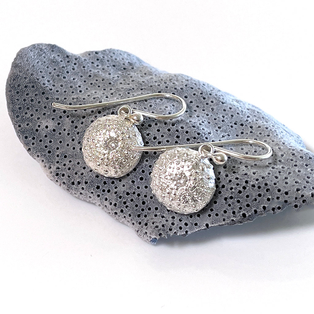 Handcrafted Medium Sea Urchin Gem Earrings featuring textured silver design inspired by Australian beach urchins with handset stone. Shown against neutral background and shell."