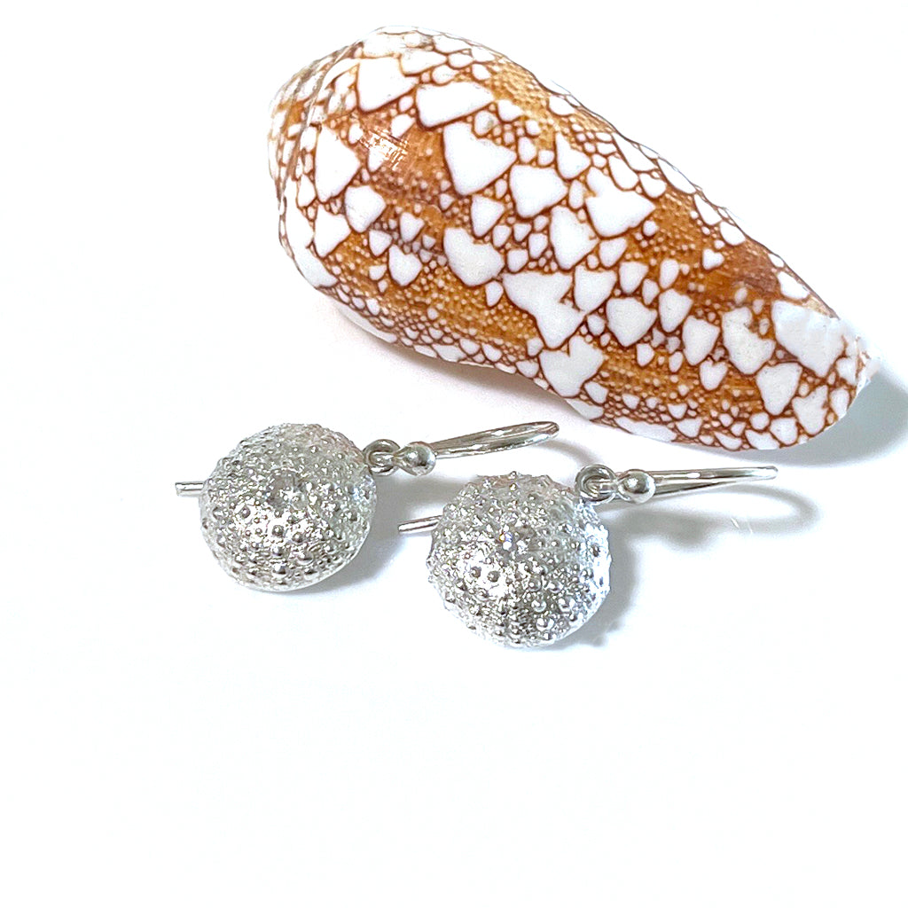 Handcrafted Medium Sea Urchin Gem Earrings featuring textured silver design inspired by Australian beach urchins with handset stone. Shown against neutral background and shell."