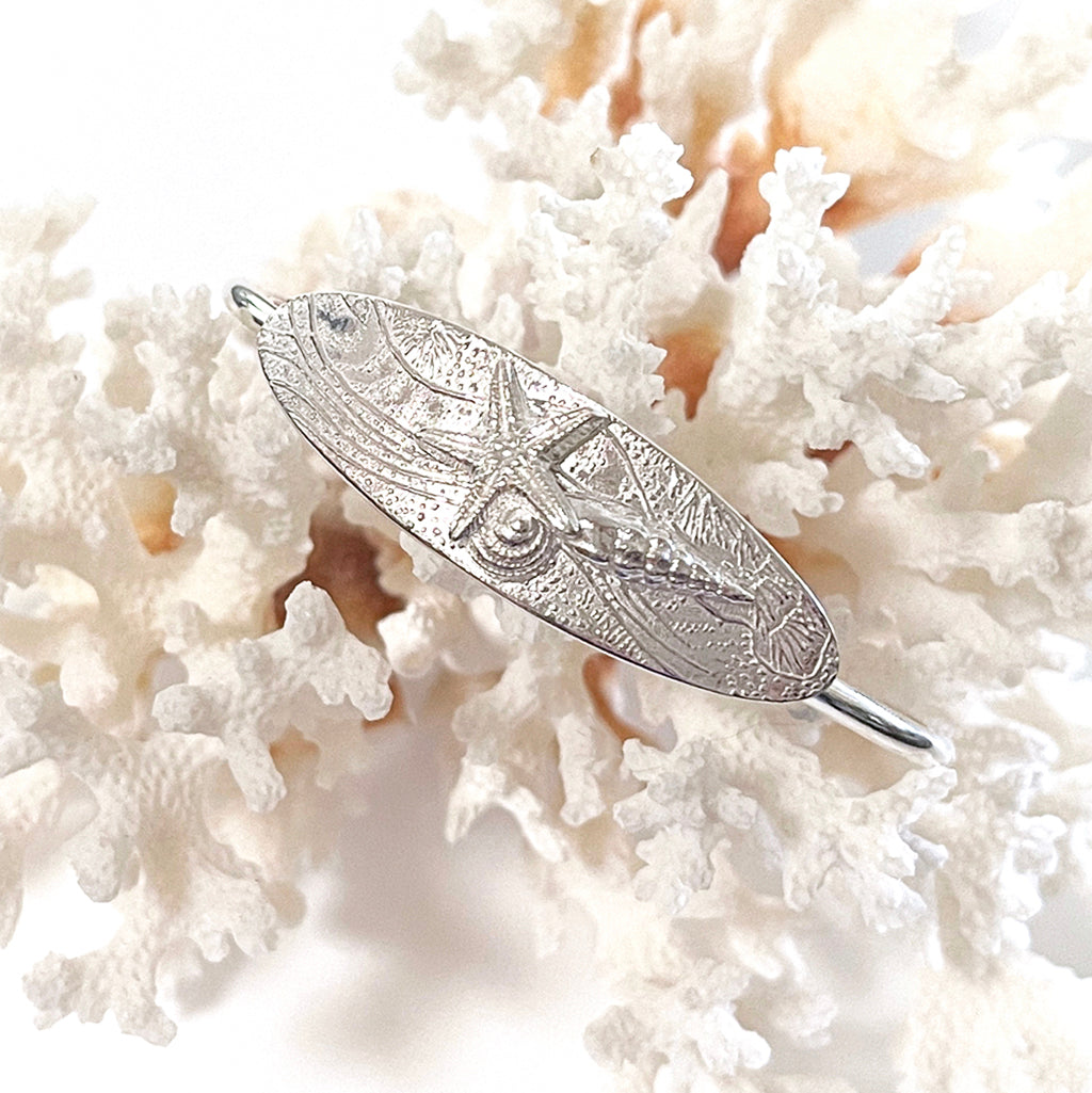 Ocean Magic Cuff featuring a pure silver shell design with coral background