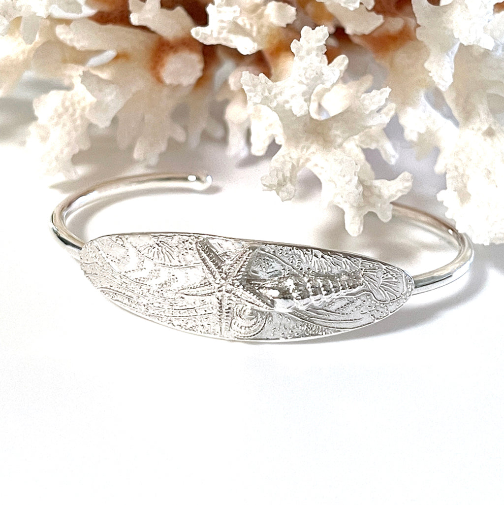Ocean Magic Cuff featuring a pure silver shell design with coral background