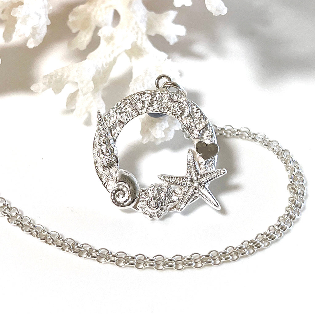 Close-up of handcrafted Heart Reef Coral Necklace showcasing intricate shell details, displayed against a piece of natural coral.
